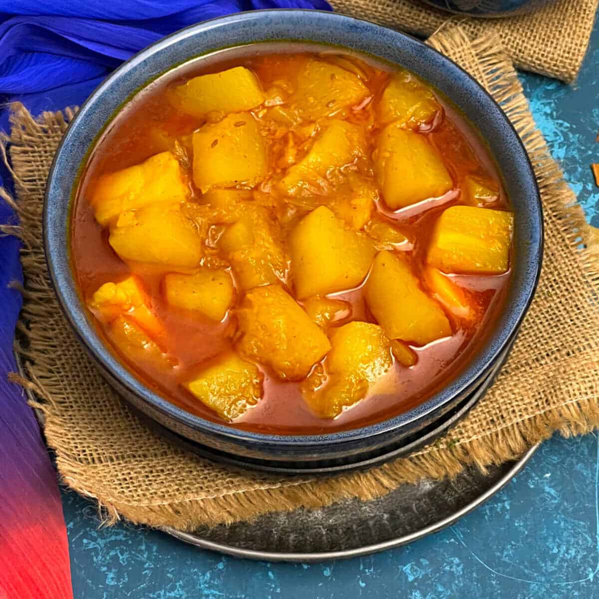 Papaya potato curry placed in a blue bowl.