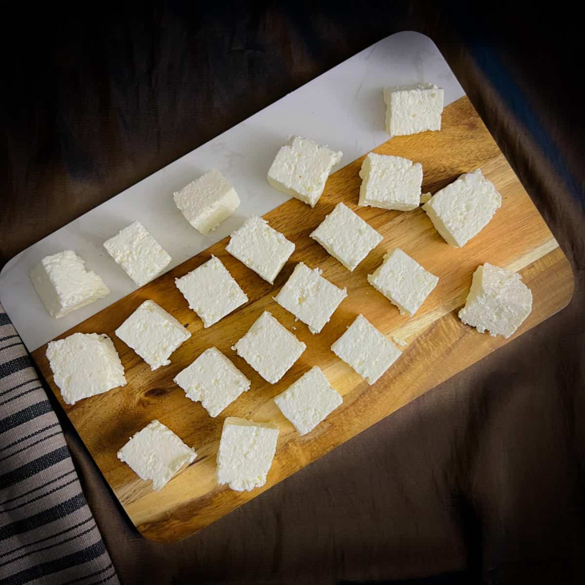Paneer cubes placed on a wooden board.