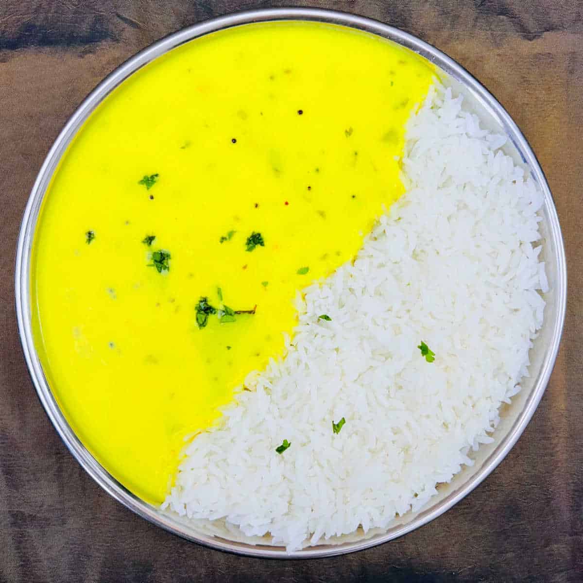 Gujarati kadhi served with rice on a steel plate.
