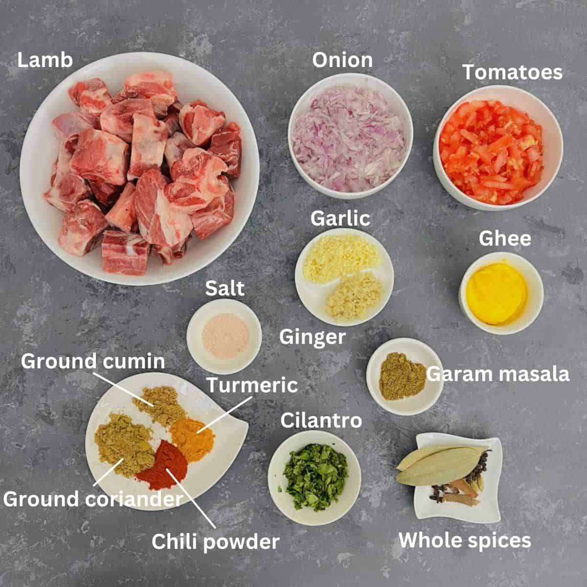 Ingredients to make lamb curry placed on a grey board.