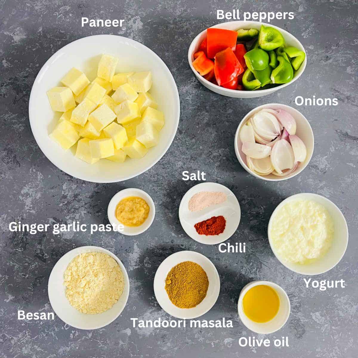 Ingredients needed to make paneer tikka placed on a grey surface.