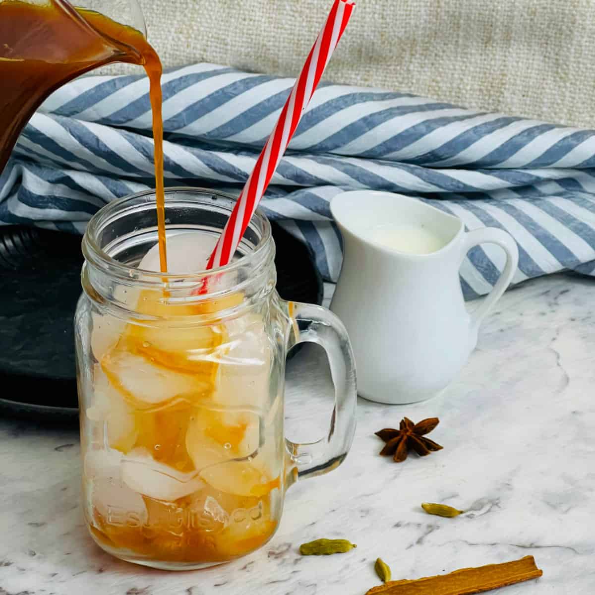 Step showing adding chai concentrate on ice cubes placed in a glass mug.