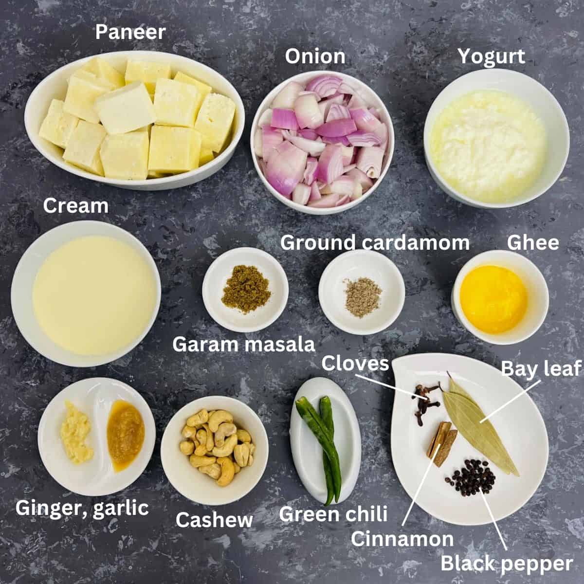 Ingredients to make shahi paneer placed on a grey surface.