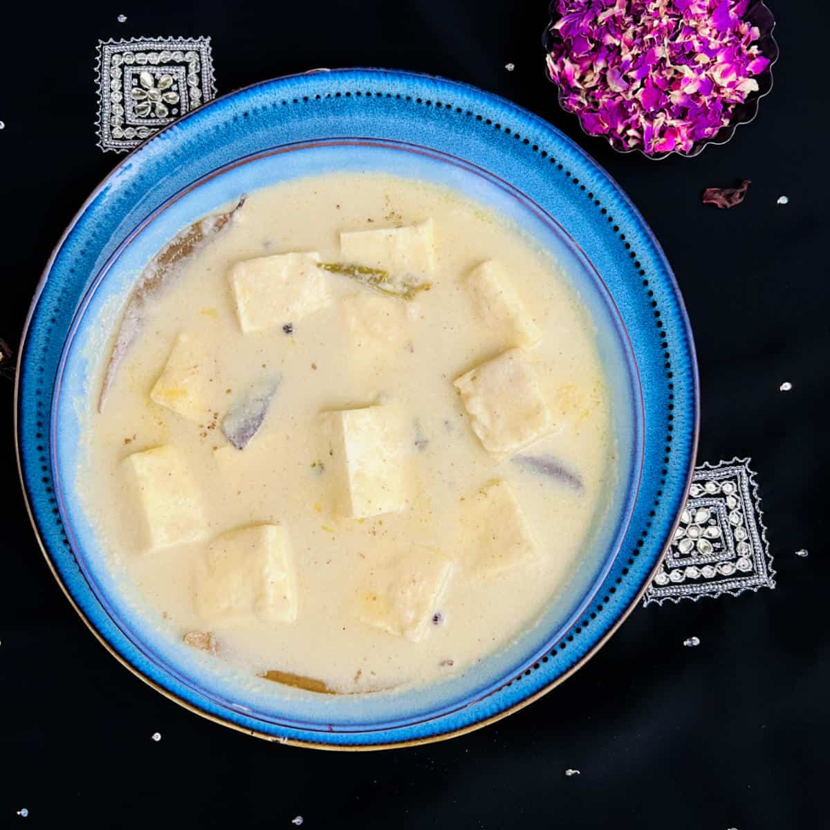 Shahi paneer placed on a black and silver surface along with rose petals.