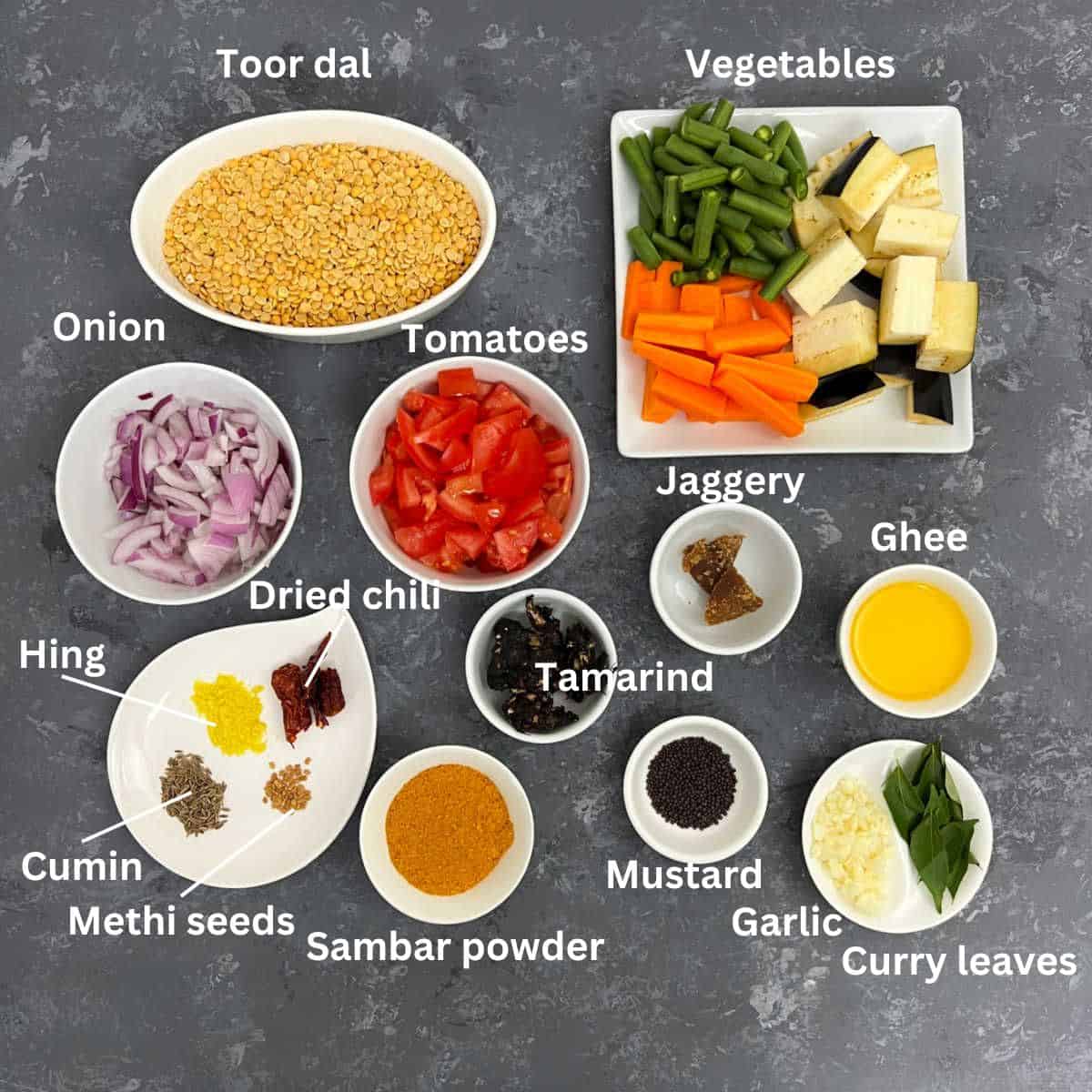 Vegetable sambar ingredients placed on a grey surface.