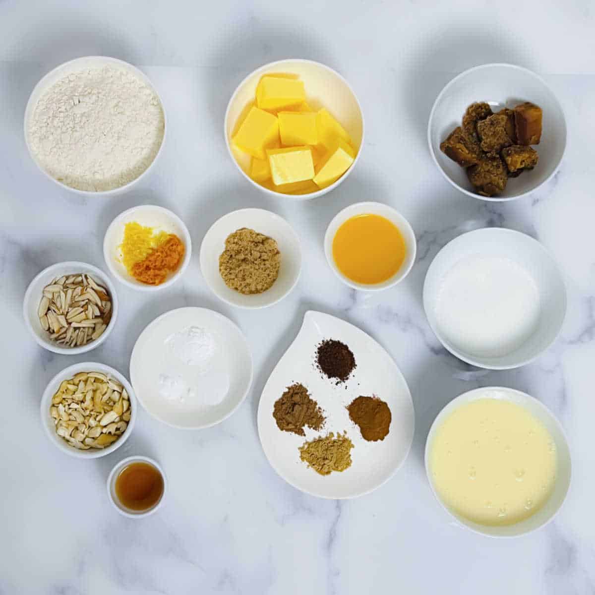 individual ingredients for plum cake laid out against a white marble background.