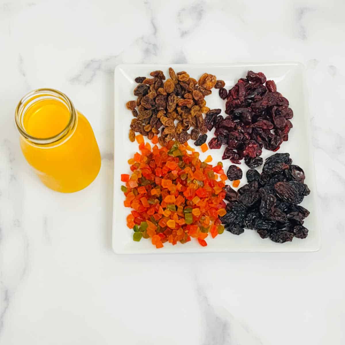 dried nuts used for soaking in the plum cake laid out on a white cutting board next to a jar of orange juice.