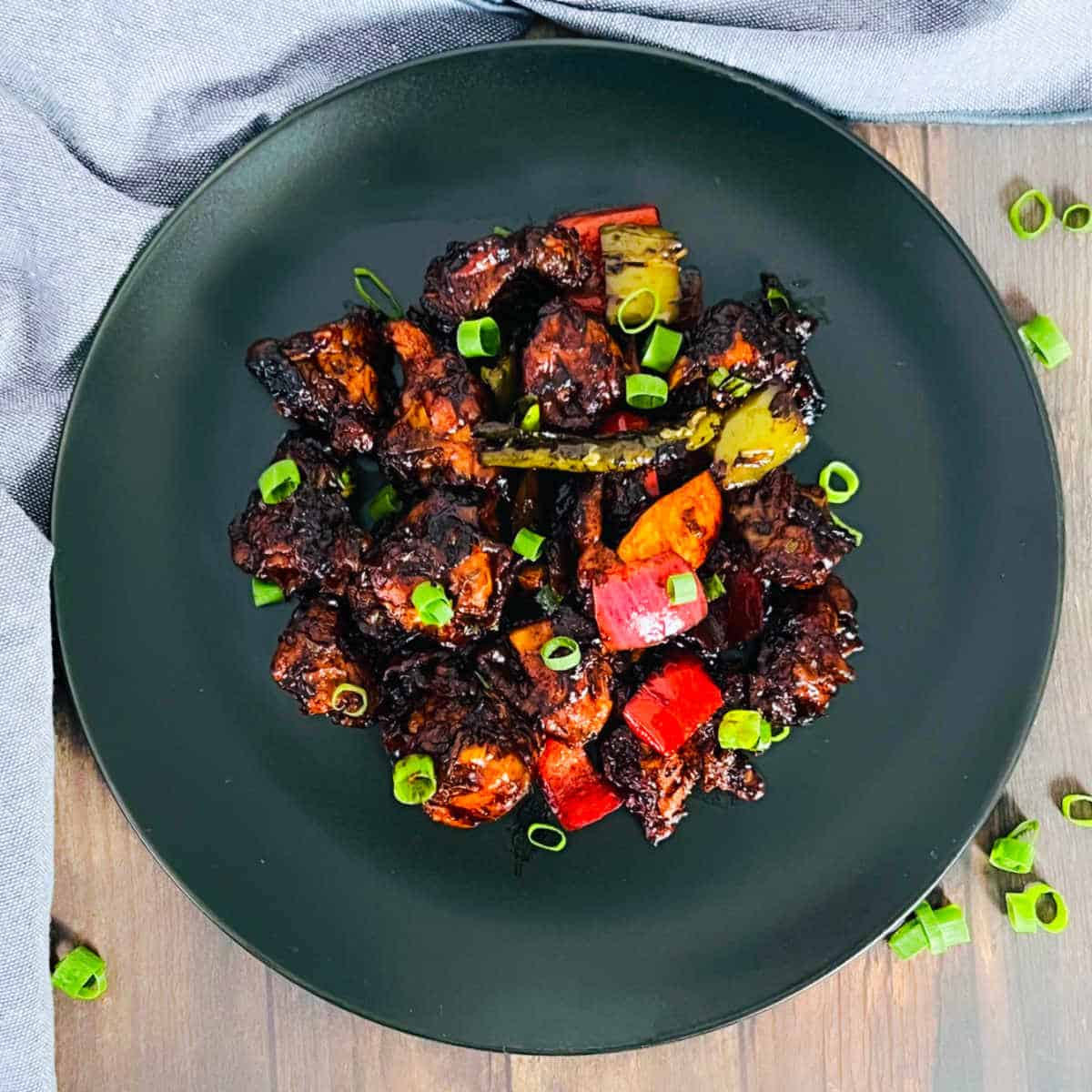 Chilli chicken garnished with green onions and placed on a wooden surface.