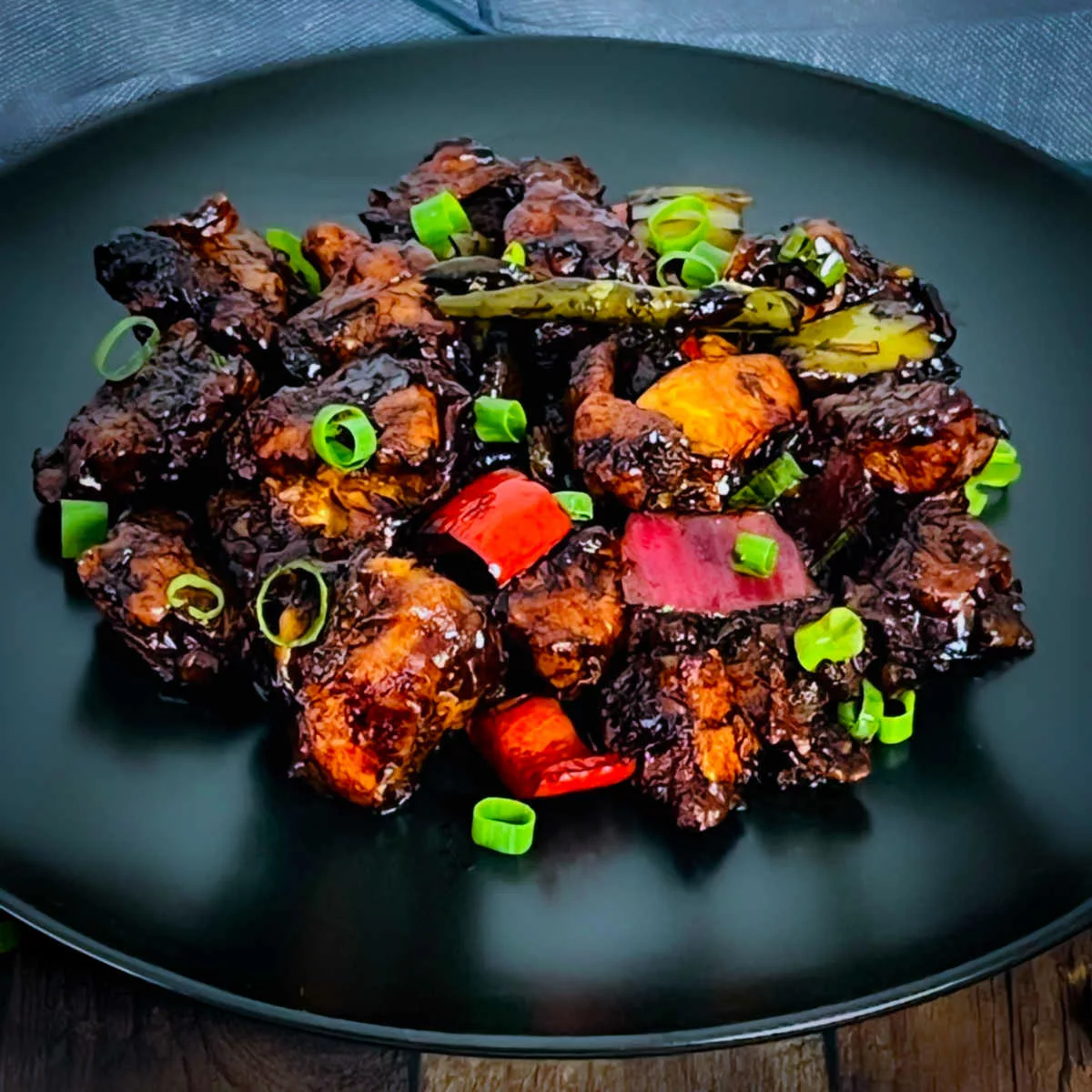 Indo-Chinese chili chicken placed on a black plate.