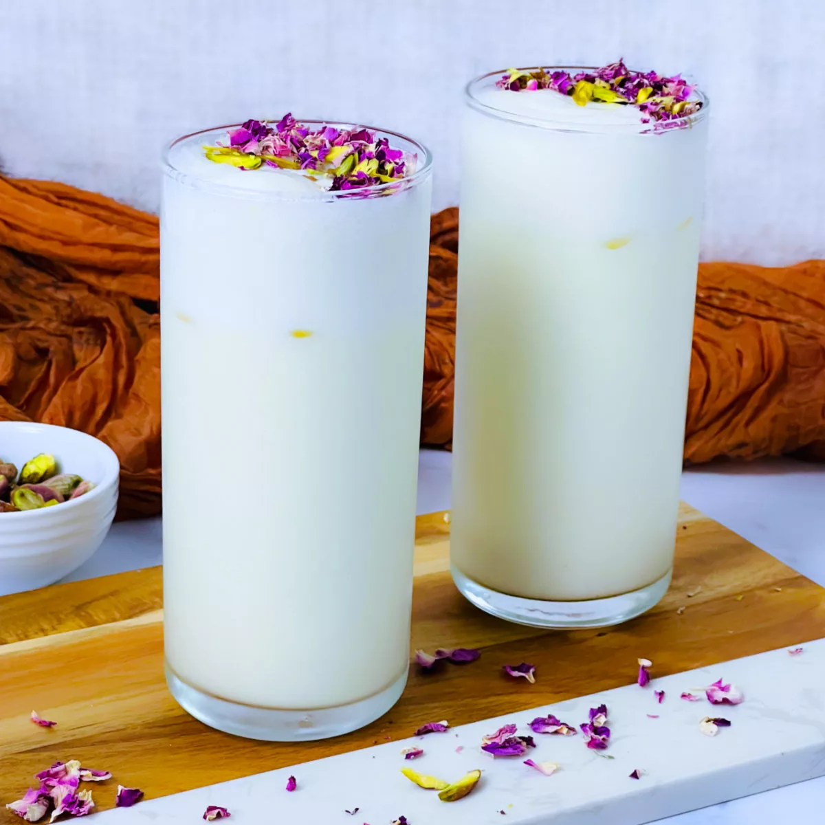 Tall glasses of lassi placed on a marble surface.