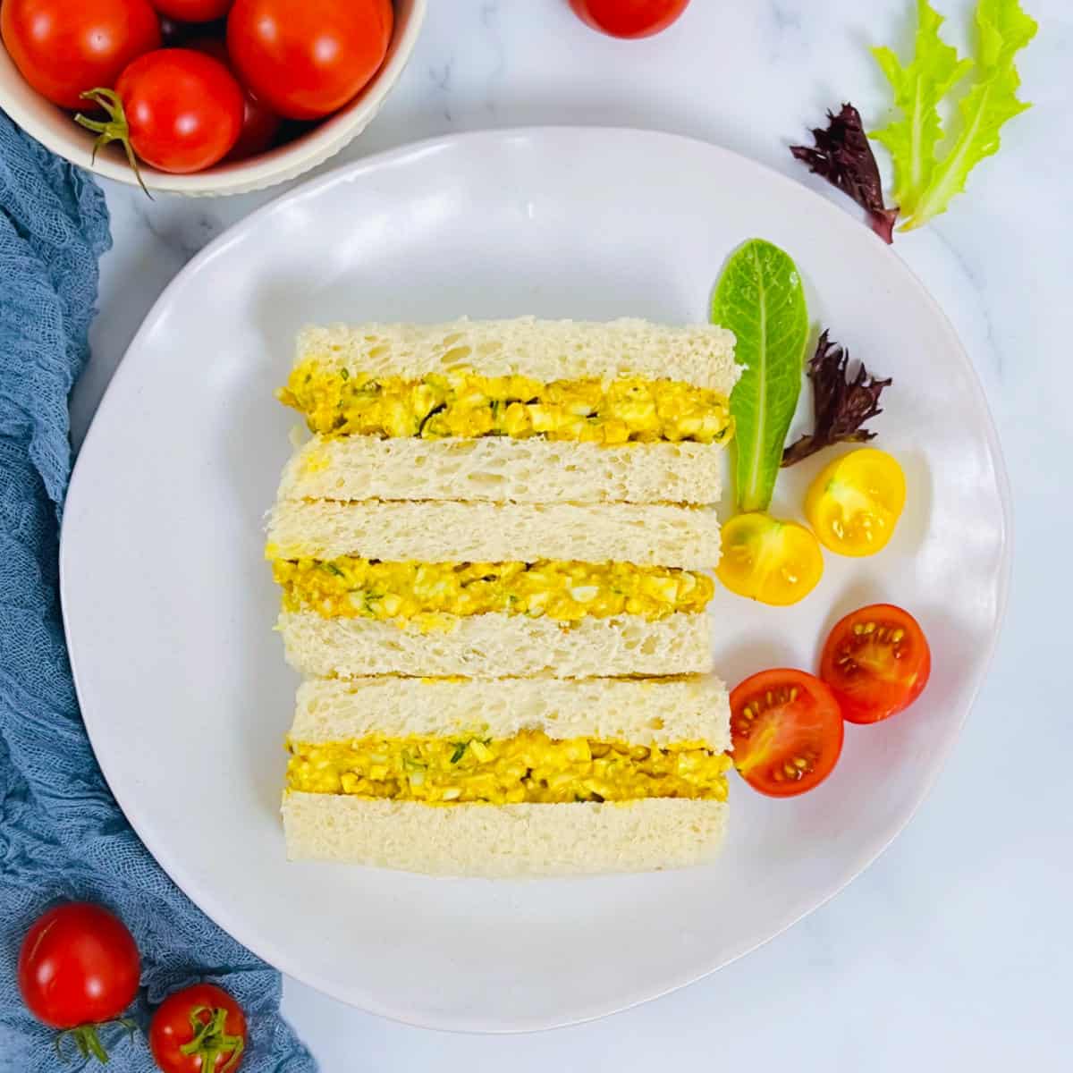 Curried egg mayo sandwich on a white plate with cherry tomatoes.