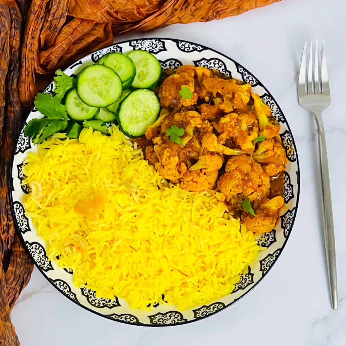 Saffron rice served with cauliflower curry and salad on a white plate.