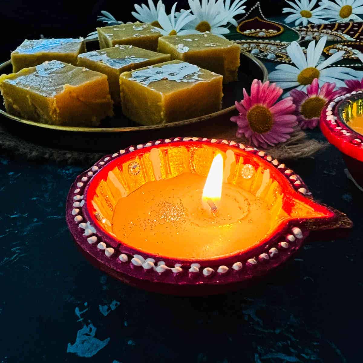Diwali diya with mohanthal in the background.