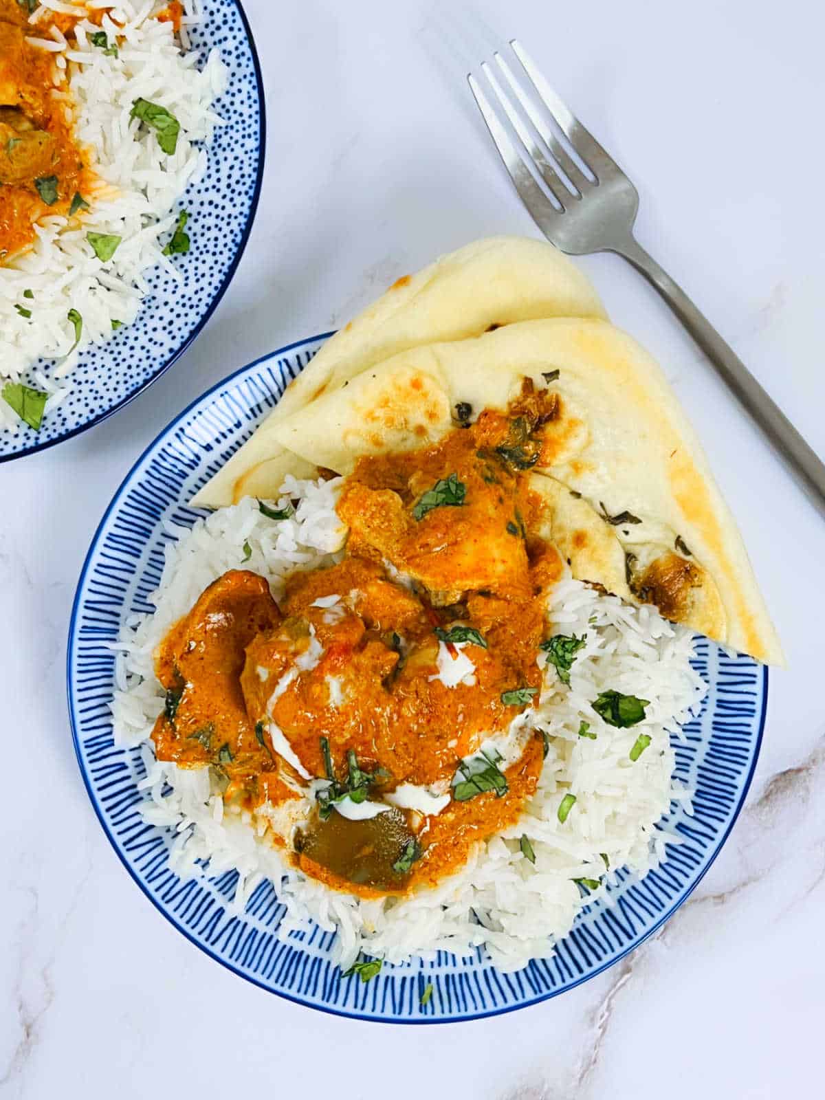 Chicken tikka masala on a bed of rice and naan on a blue plate.