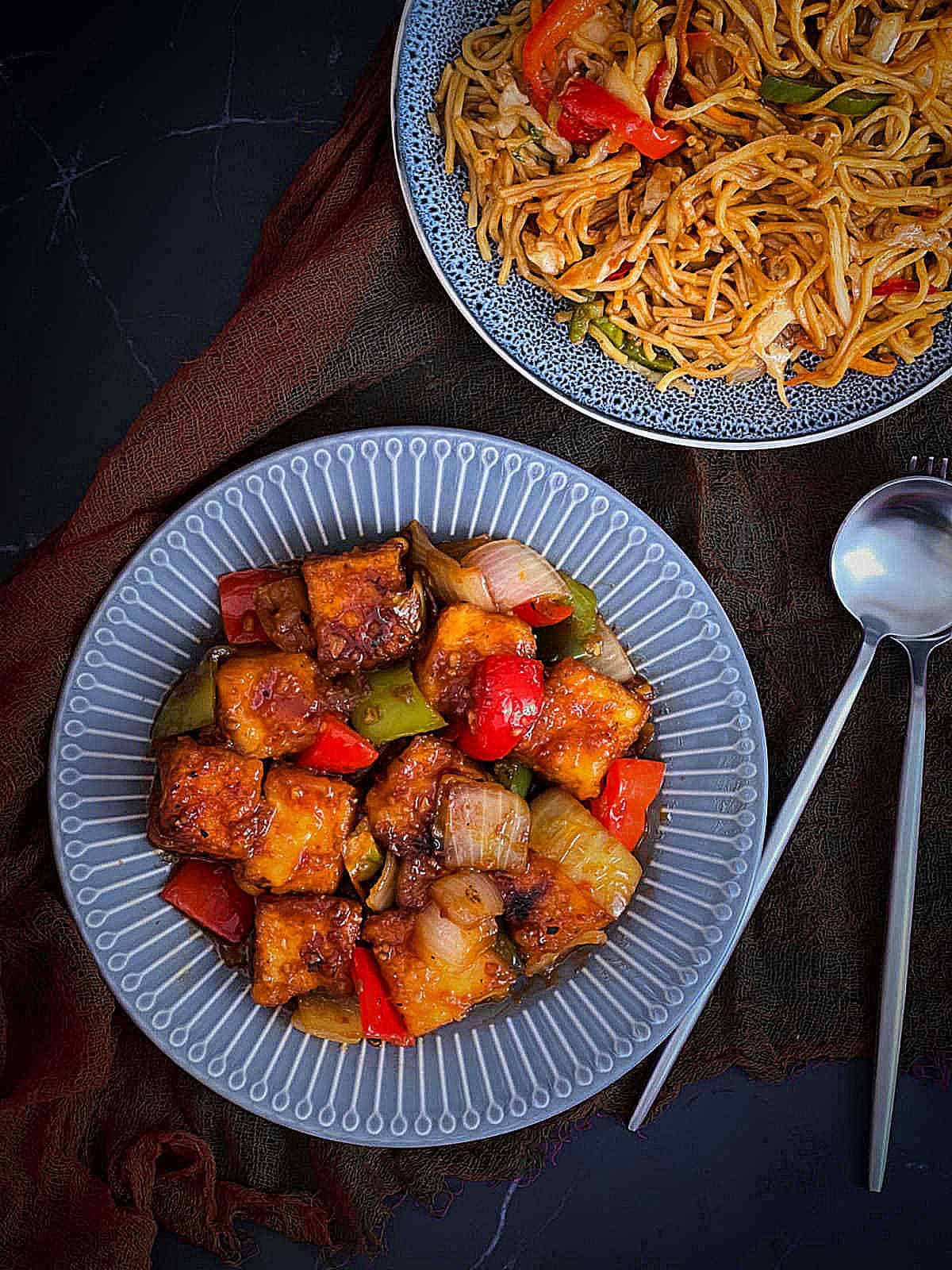 Chilli paneer served with Hakka noodles on a grey plate.