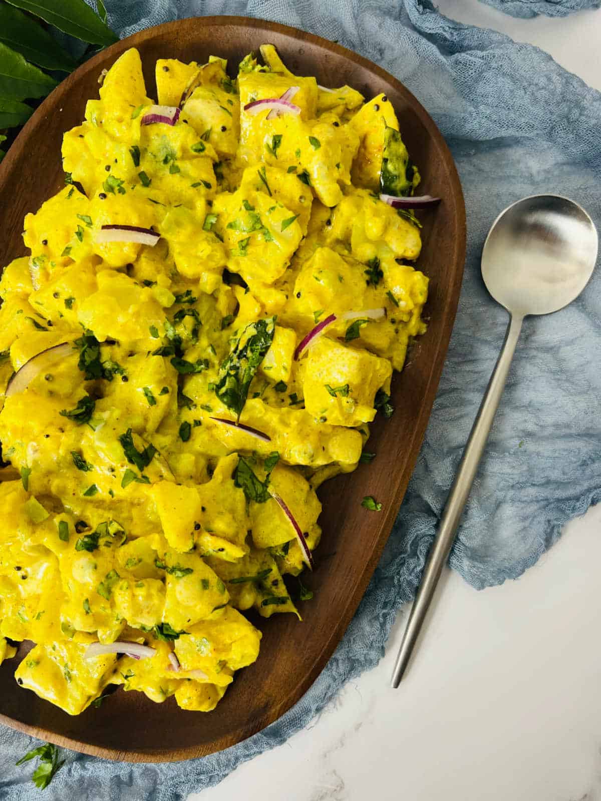 Curried potato salad served on a wooden plate.