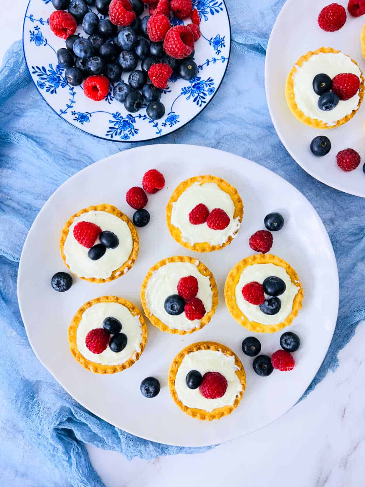 Shrikhand tarts placed on a white plate with berries in the background.