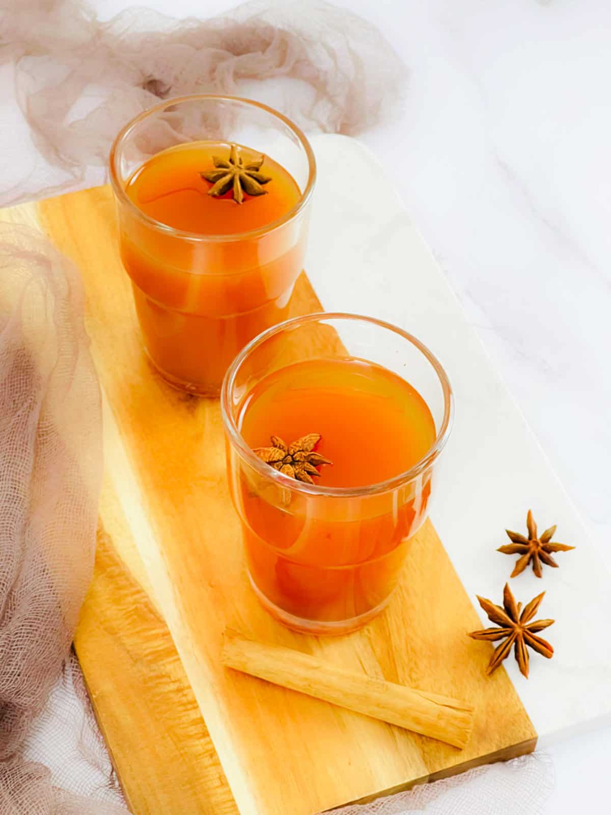 Chai hot toddy glass topped with star anise and placed on a wooden board.