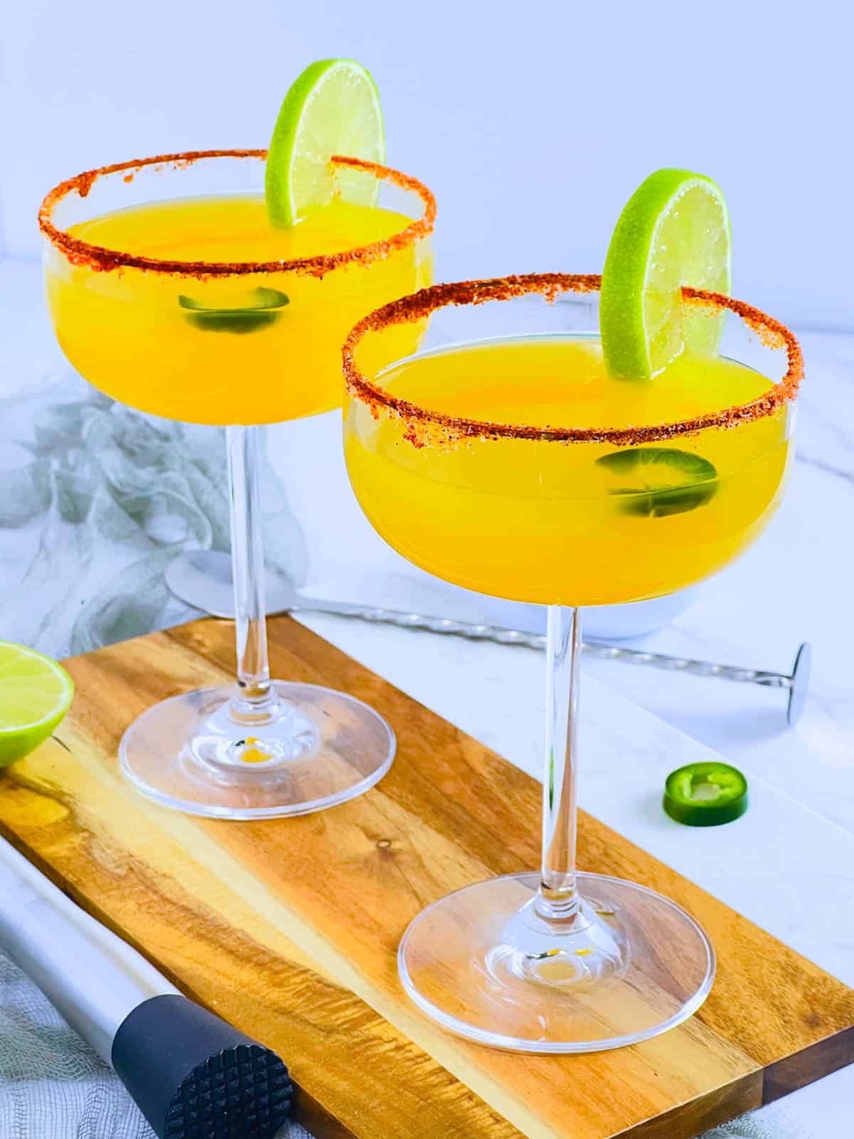 Spicy mango margarita placed on a wooden board with jalapeno and lime.