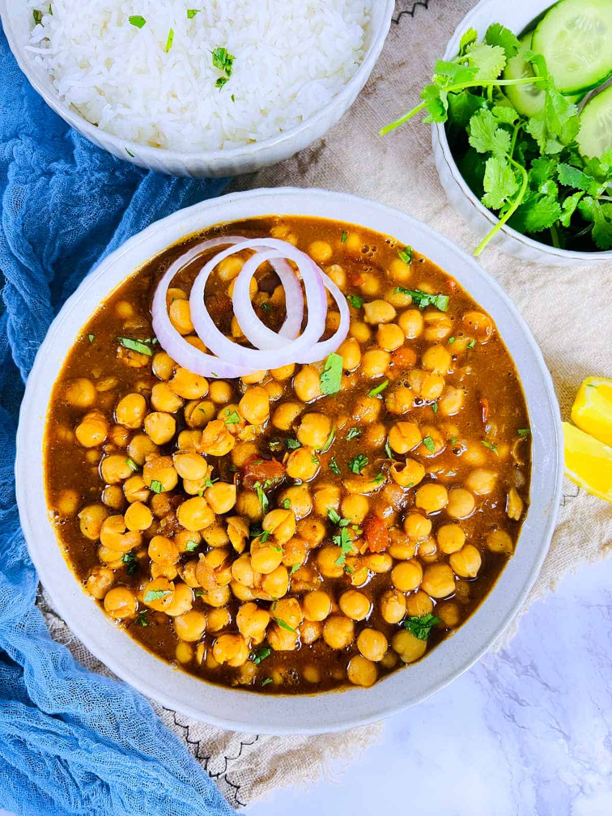 Chana masala in a white bowl along with rice and salad.