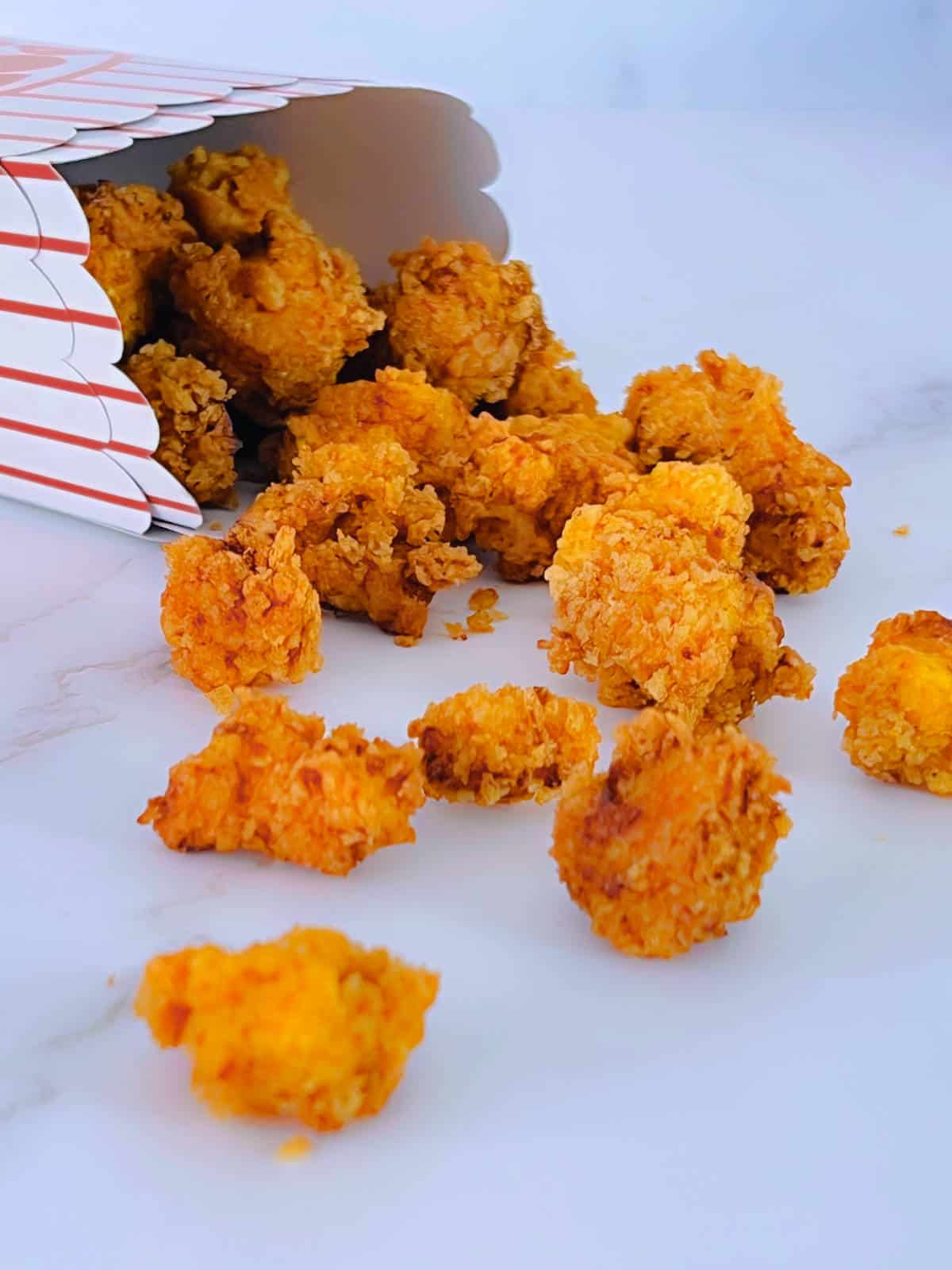 Popcorn chicken falling off from a paper box on a marble background.