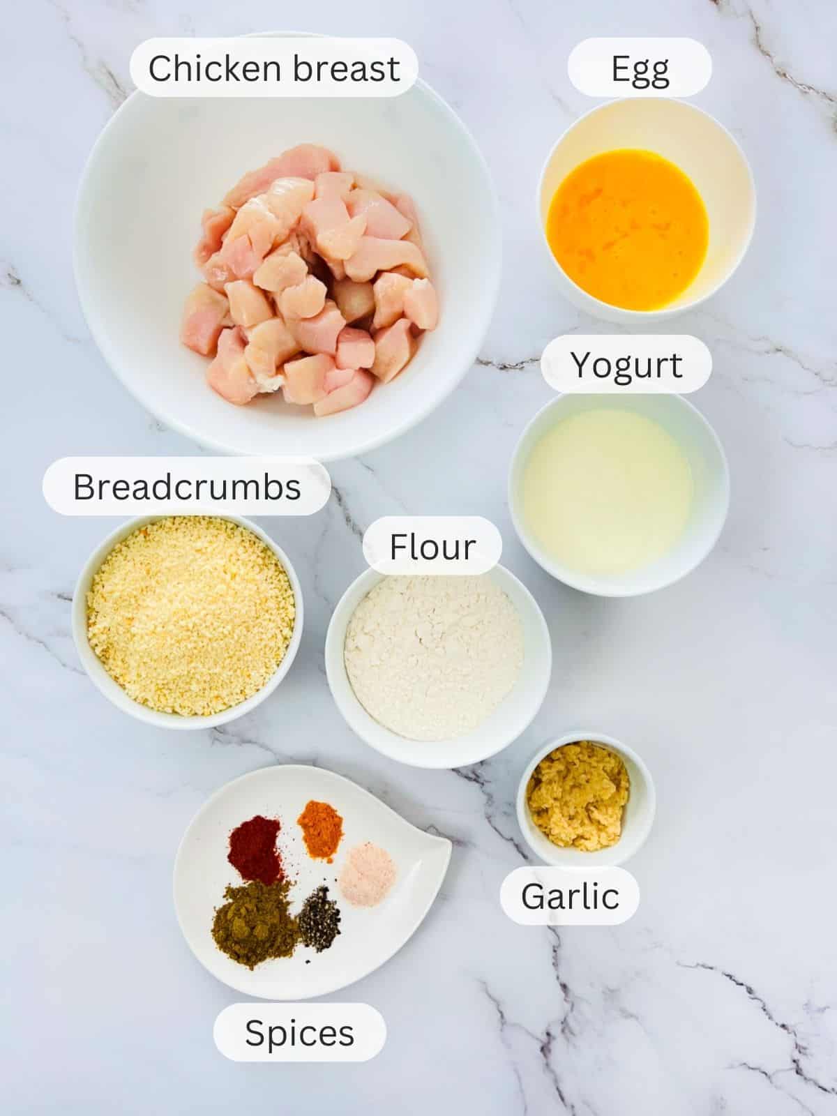 Ingredients to make chicken nuggets placed on a marble surface.