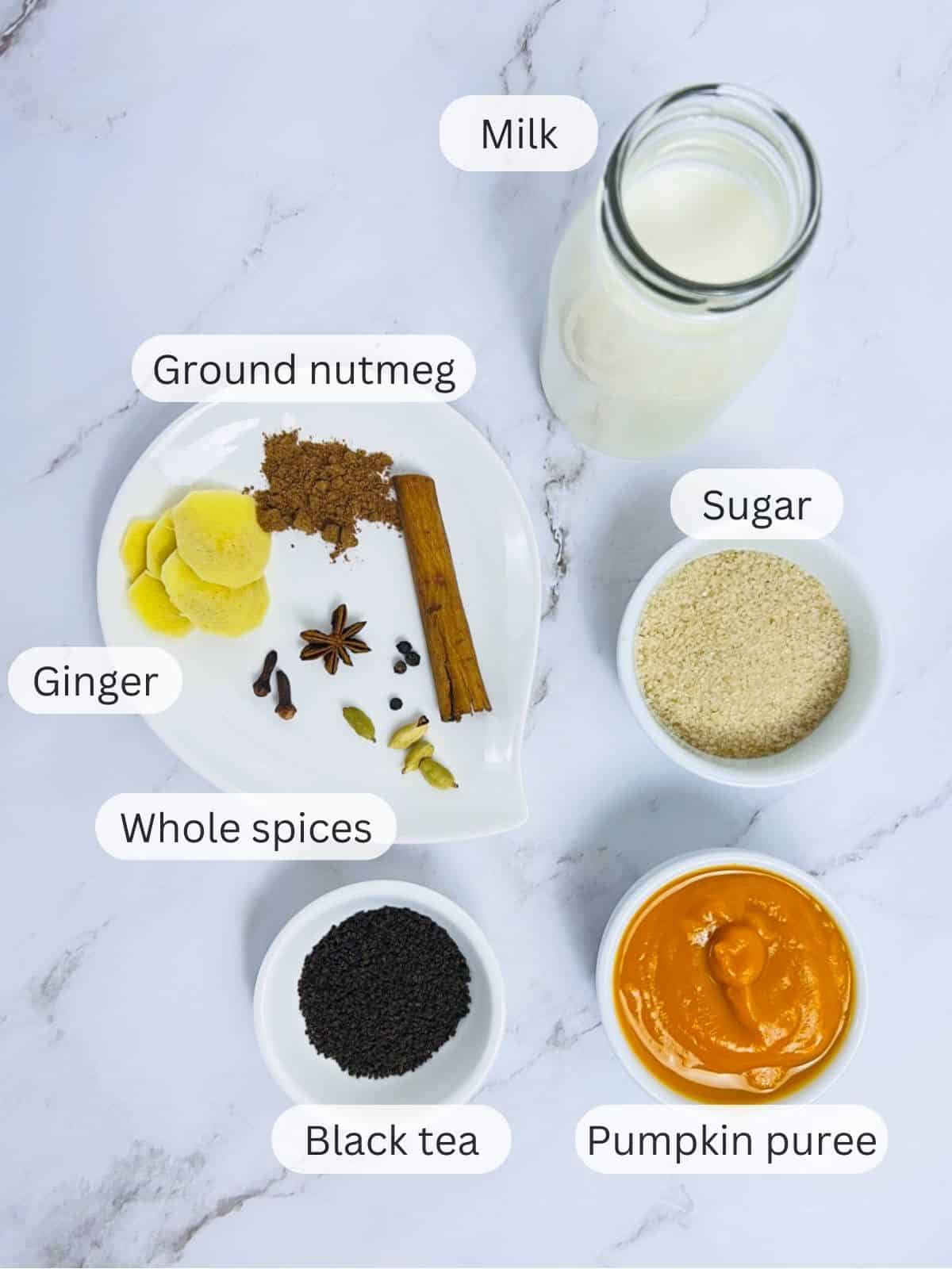 Ingredients to make pumpkin chai latte placed on a marble surface.