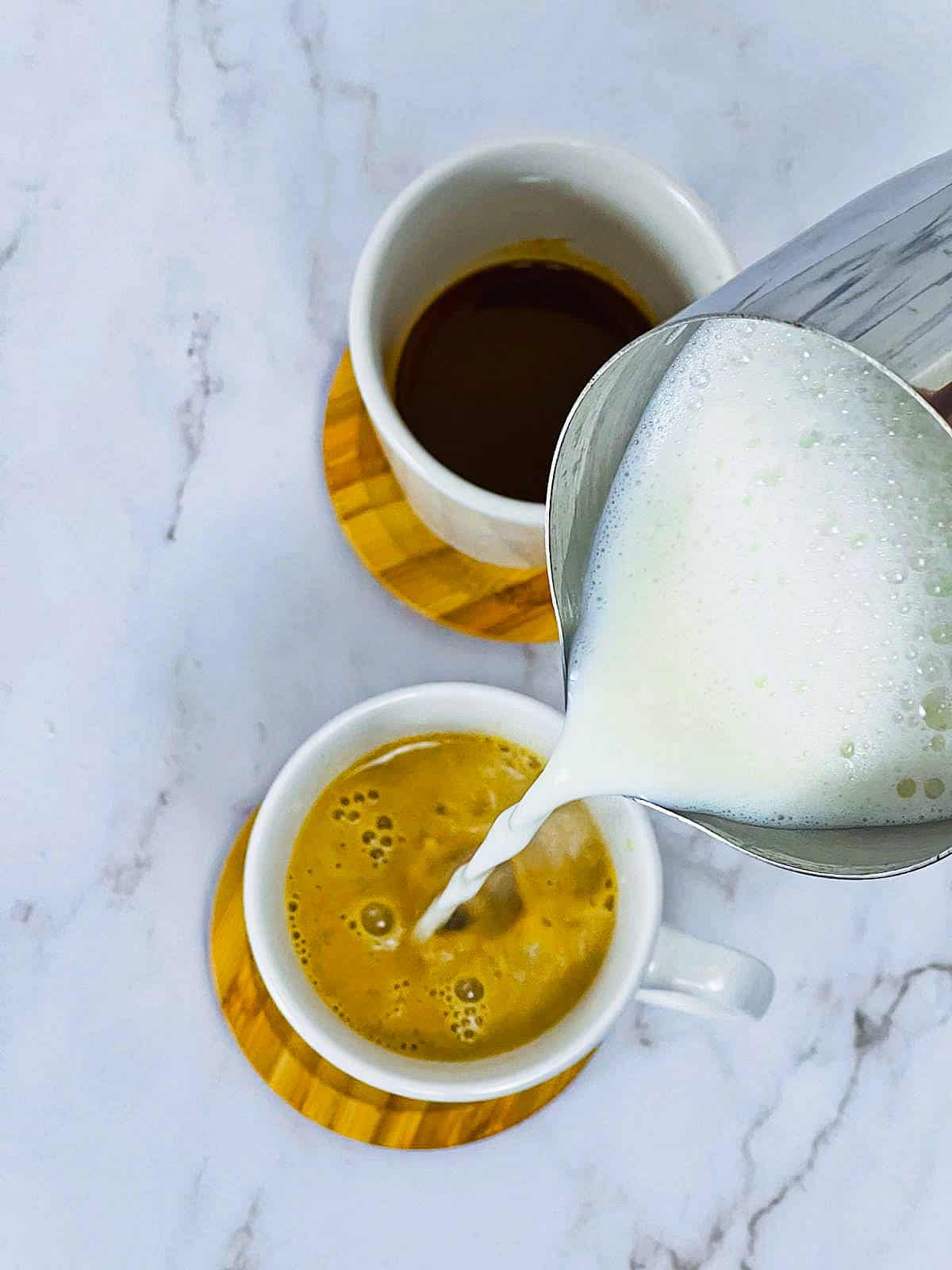 Pouring frothy milk into cups with pumpkin chai concentrate.