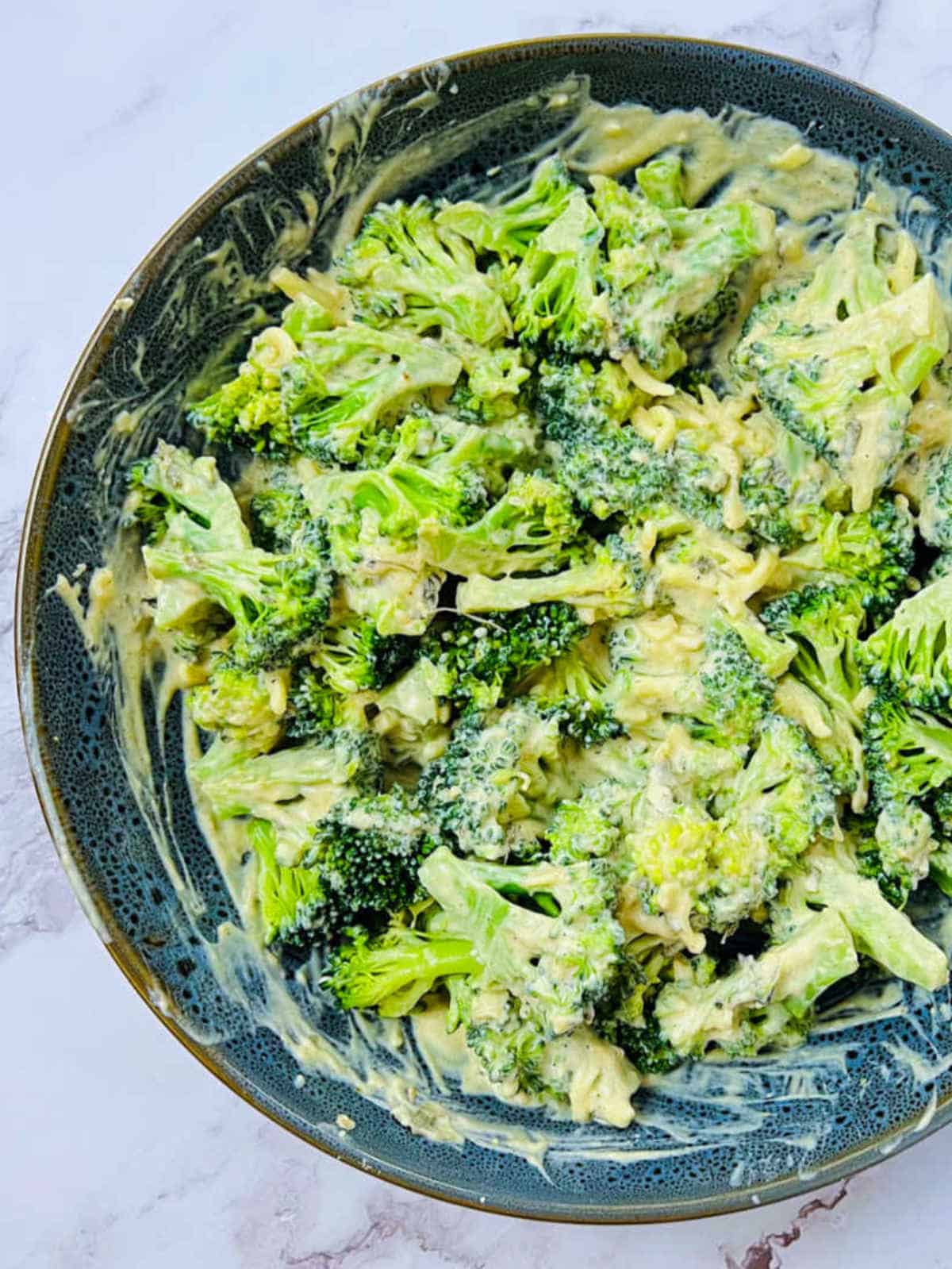 Marinated broccoli florets in a grey bowl.