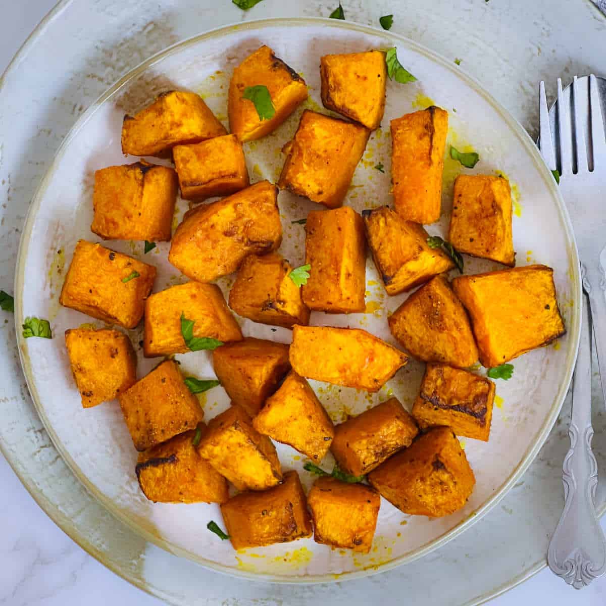 Air fryer roasted pumpkin cubes placed on a white plate.