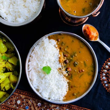 Palak sambar served with rice on a steel plate with mango pickle.
