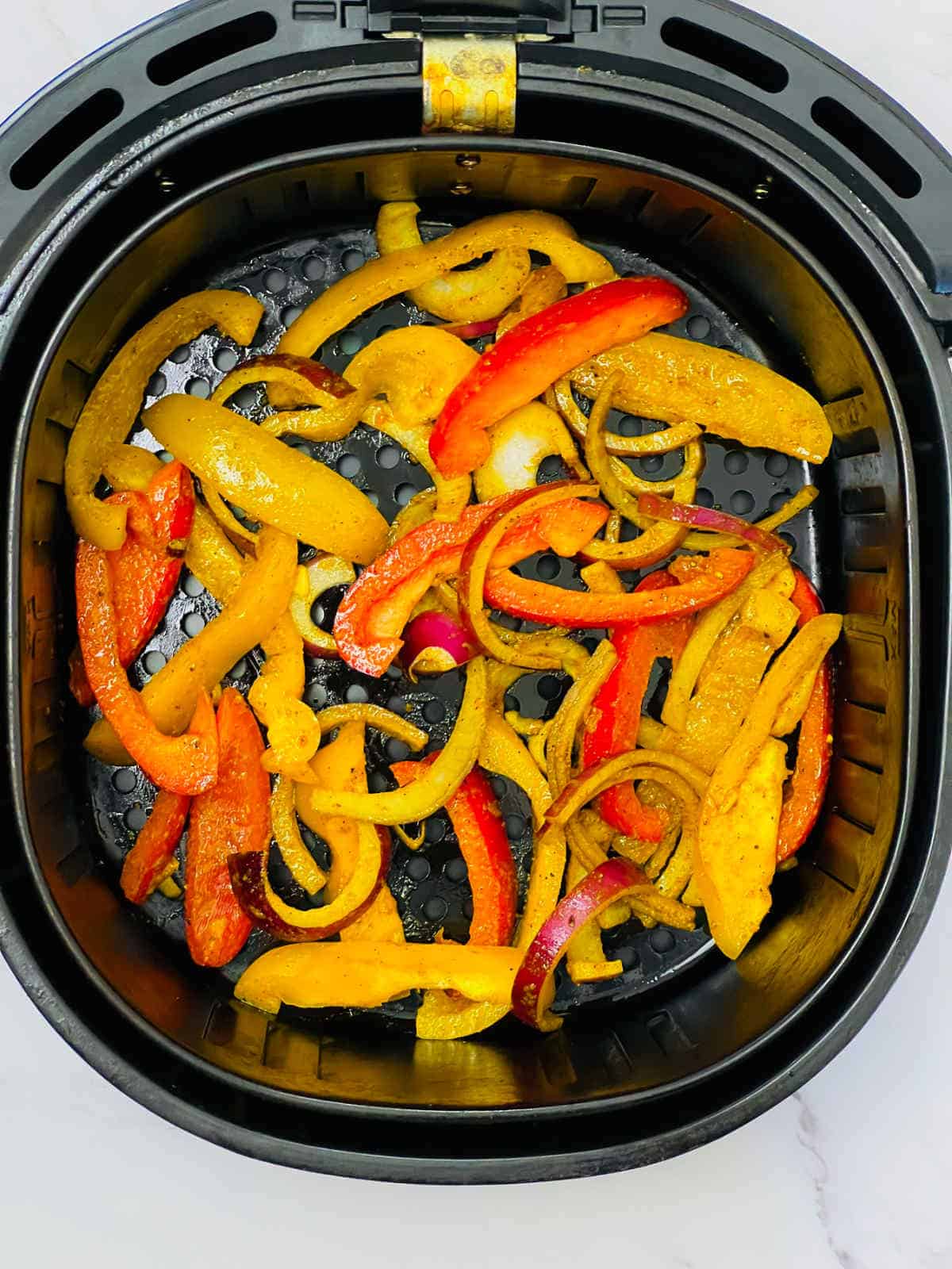 Seasoned bell peppers in air fryer basket.