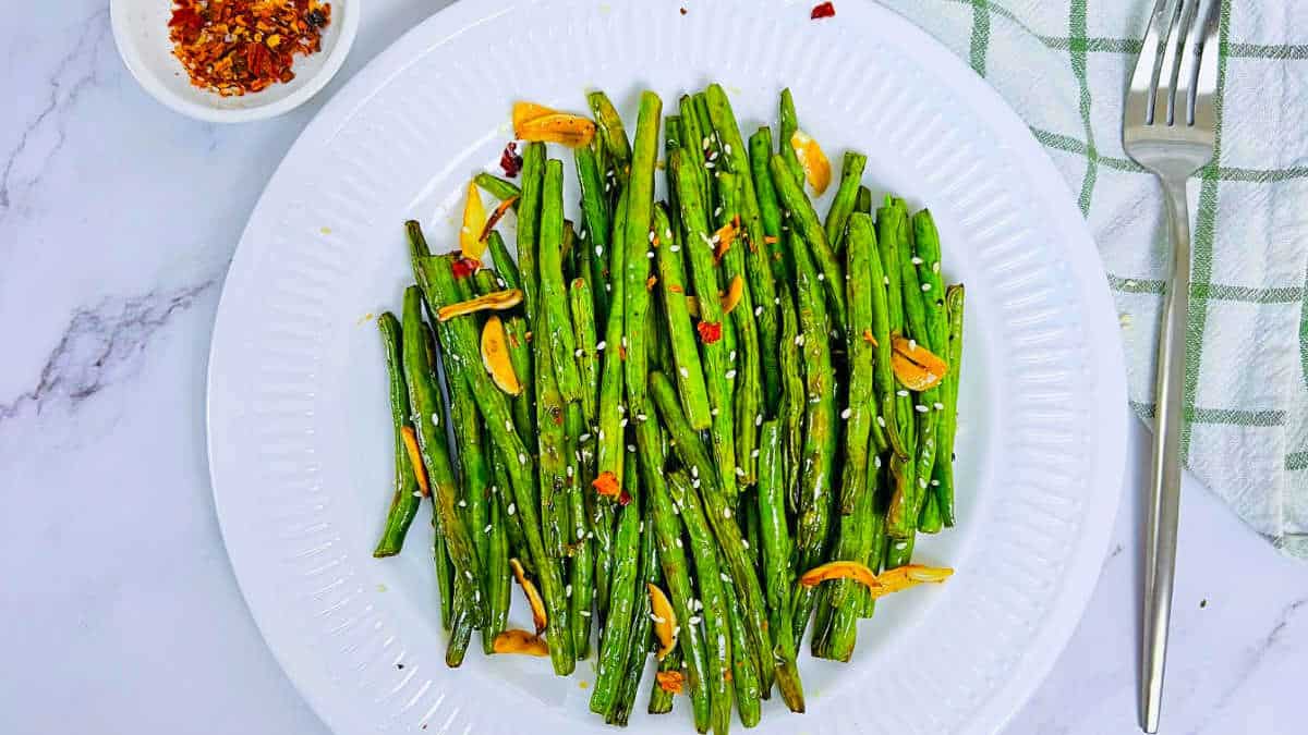 Roasted green beans served on a white plate.