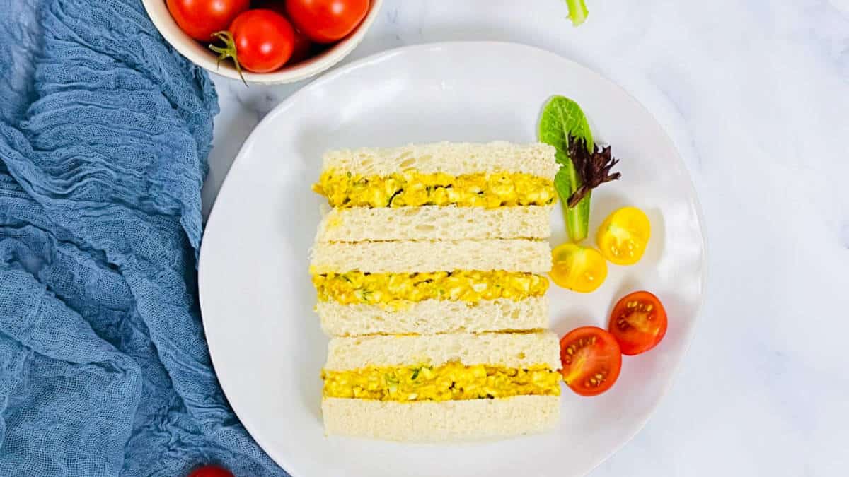 Curried egg sandwich served with tomatoes on white plate.