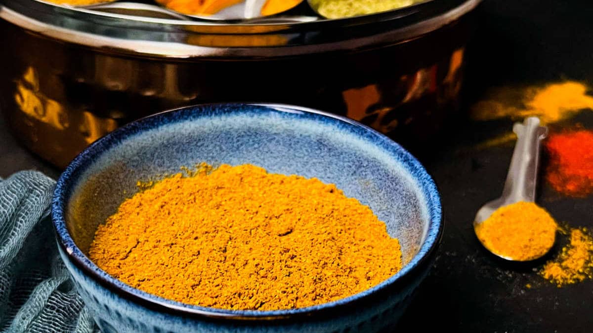 Curry powder in a bowl with whole spices in the background.