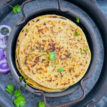Gobi paratha garnished with cilantro and placed on a black plate.