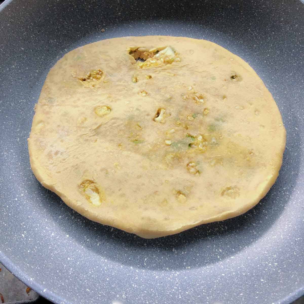 Step showing the paratha placed on a hot tava for cooking.