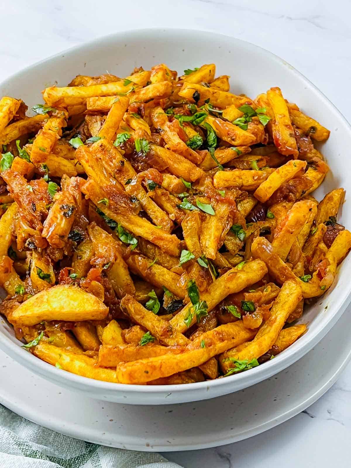 Masala fries served in a white bowl garmished with cilantro.