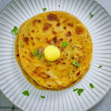 A stack of aloo paratha placed on a white plate.