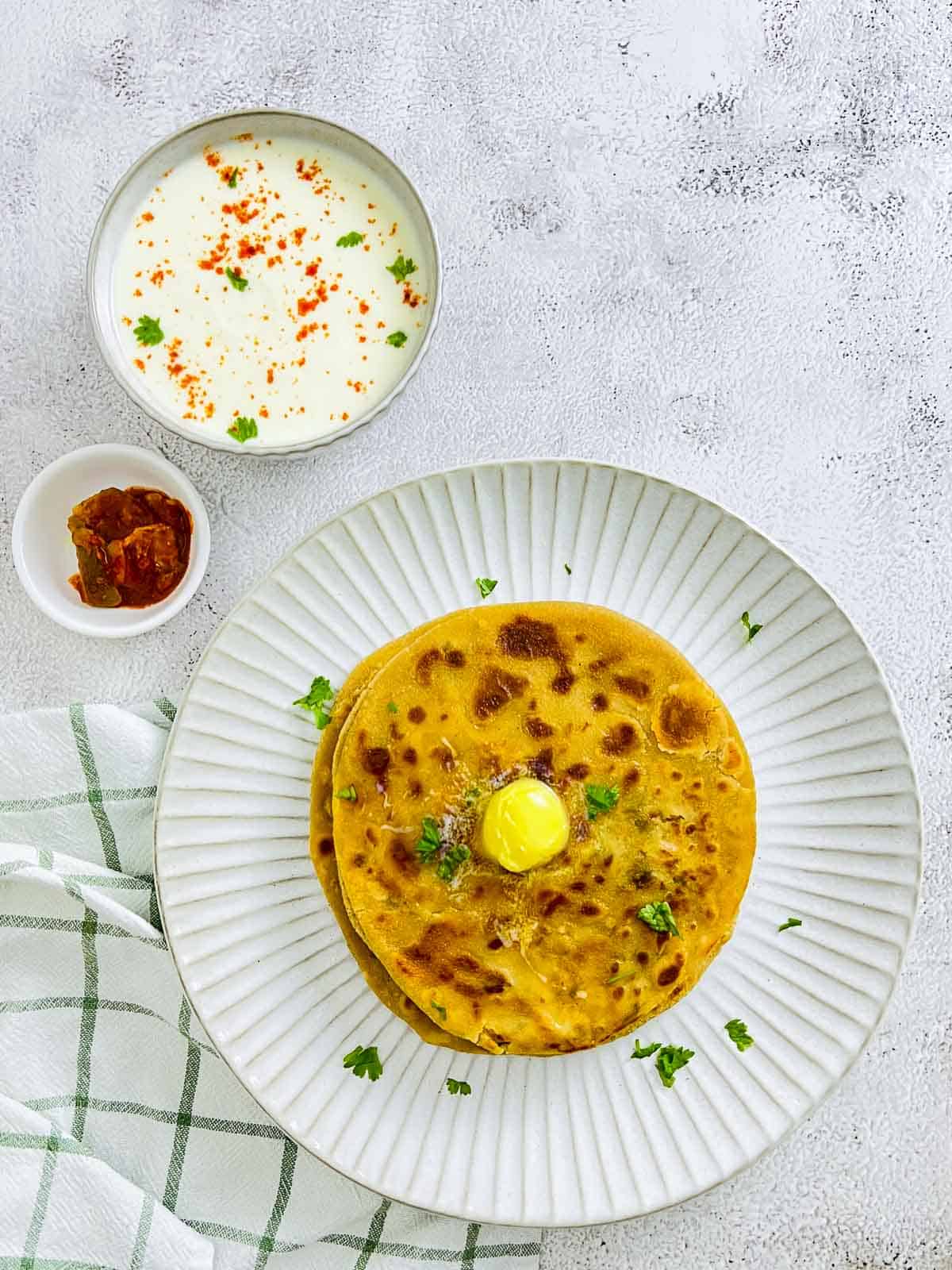 Aloo paratha topped with butter and served with yogurt and pickle.