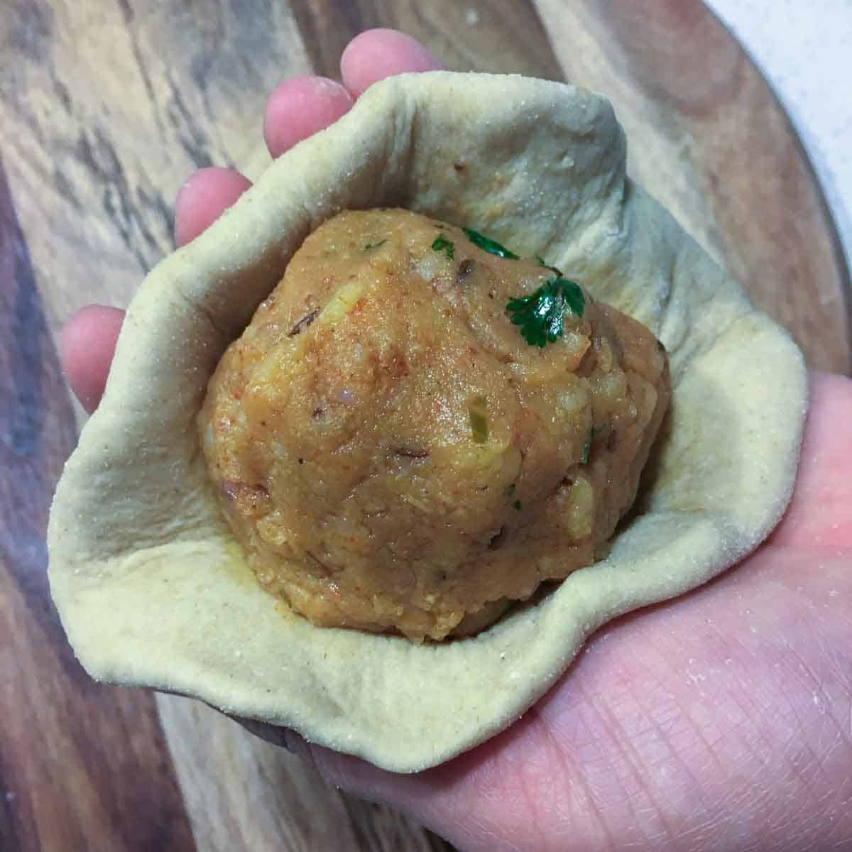 Step showing a ball of potato stuffing placed on a disc of rolled dough.