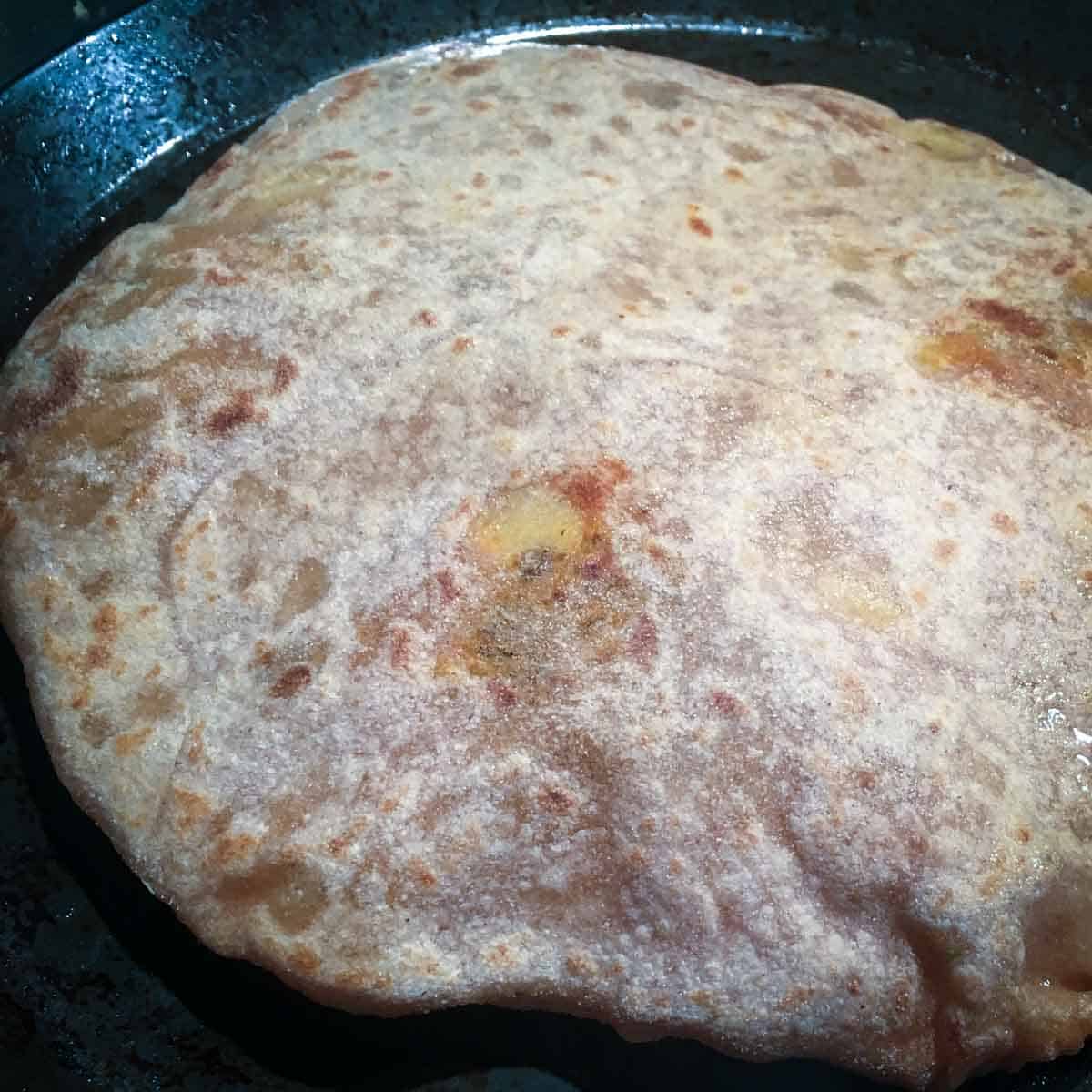 Step showing the puffing up of paratha during the cooking process.