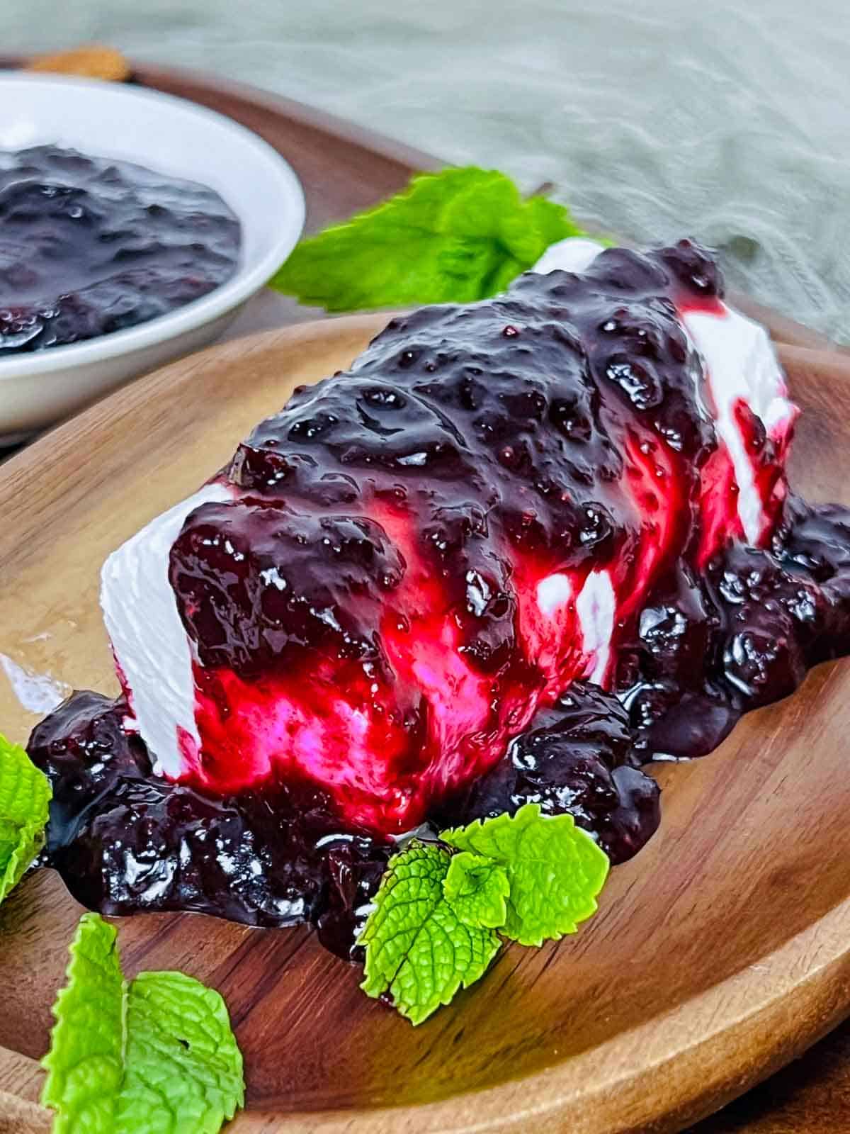 A goat cheese log placed on wooden board with blueberry chutney drizzled on top.