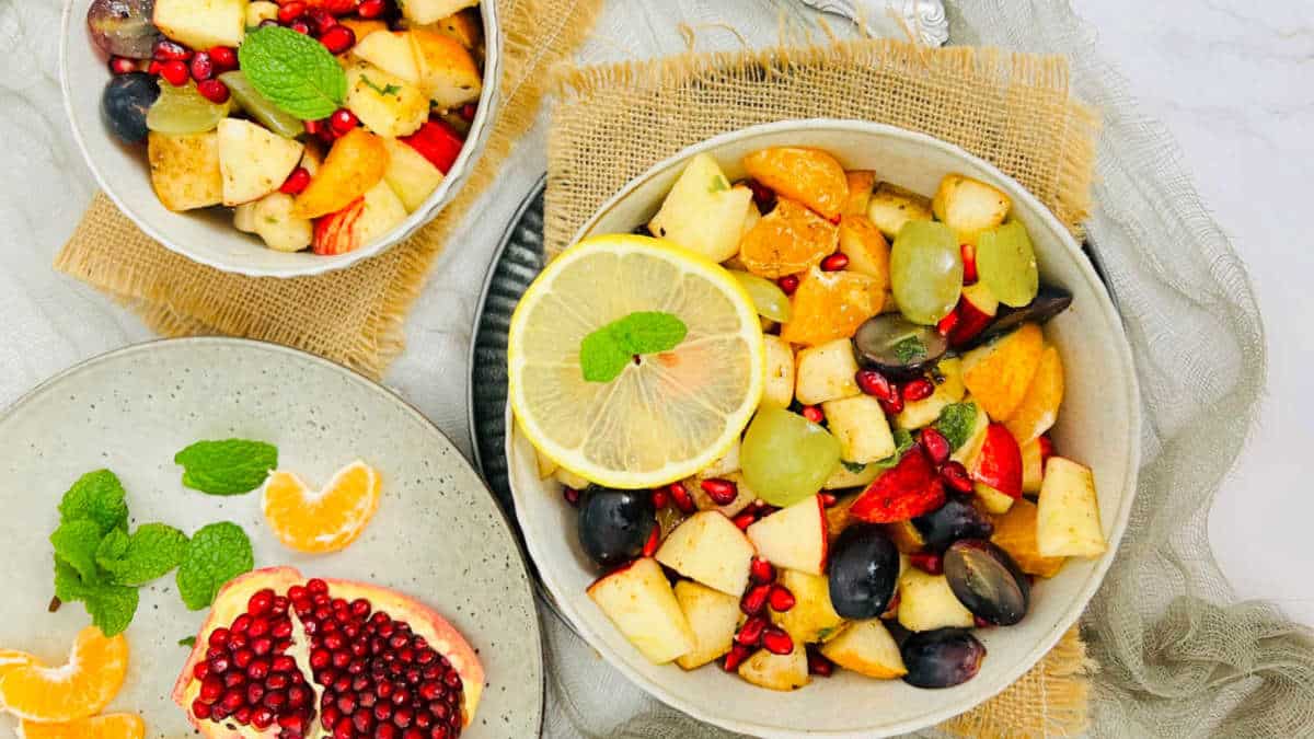 Fruit chaat in two bowls with cut fruits on a plate.