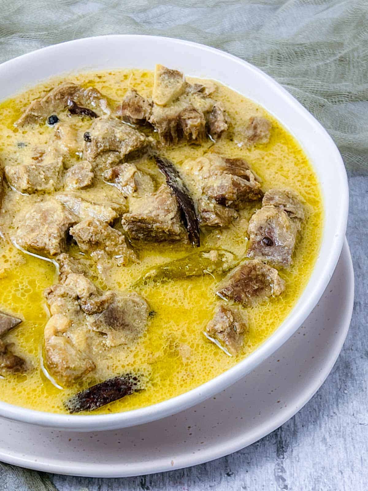 Lamb rezala in a white bowl placed on white surface.