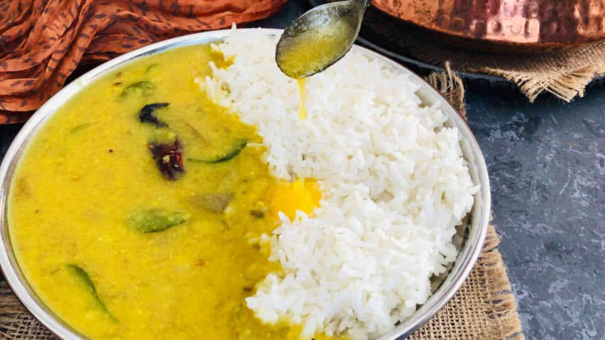 Mango dal served with rice on a steel plate with ghee being poured.