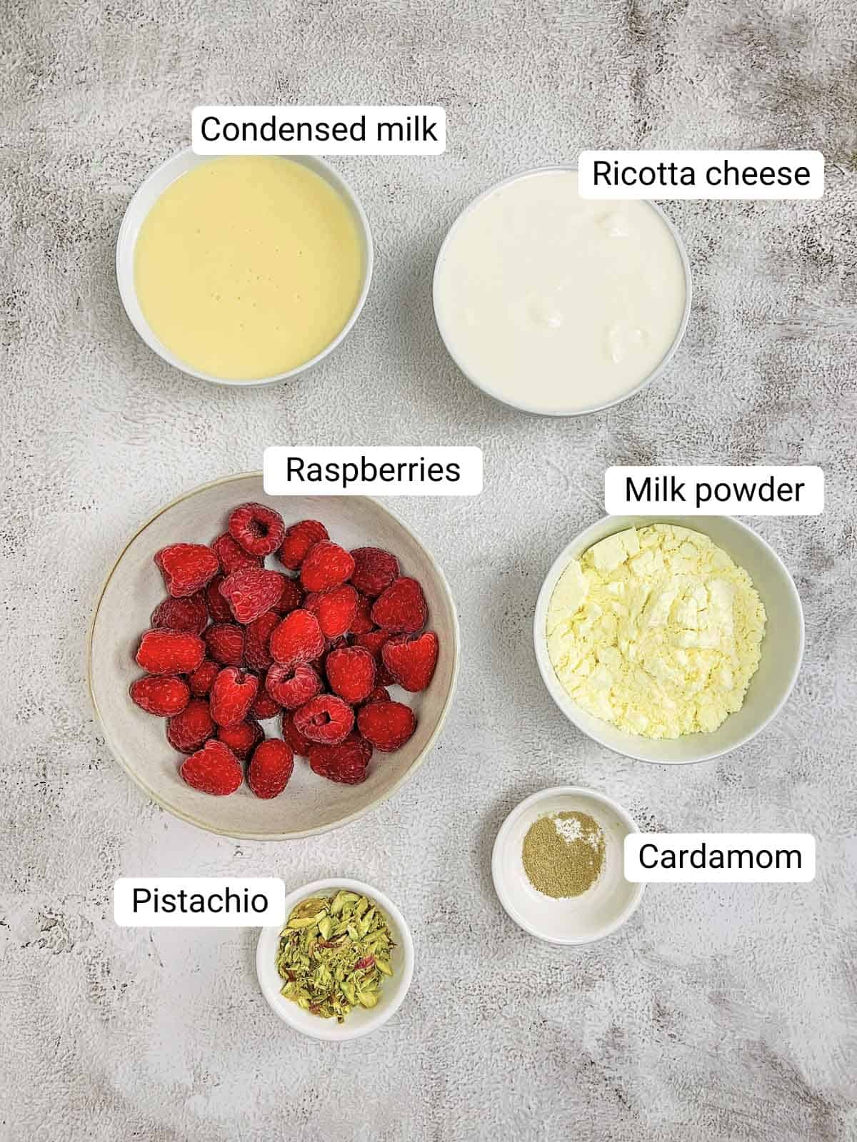Ingredients to make raspberry kalakand placed on a white surface.