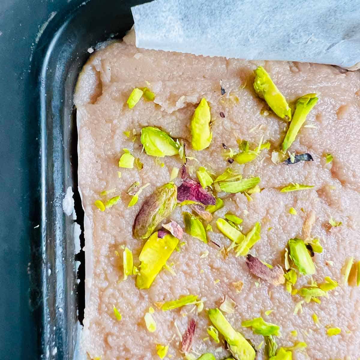 Raspberry kalakand set in a lined tin and topped with pistachio.
