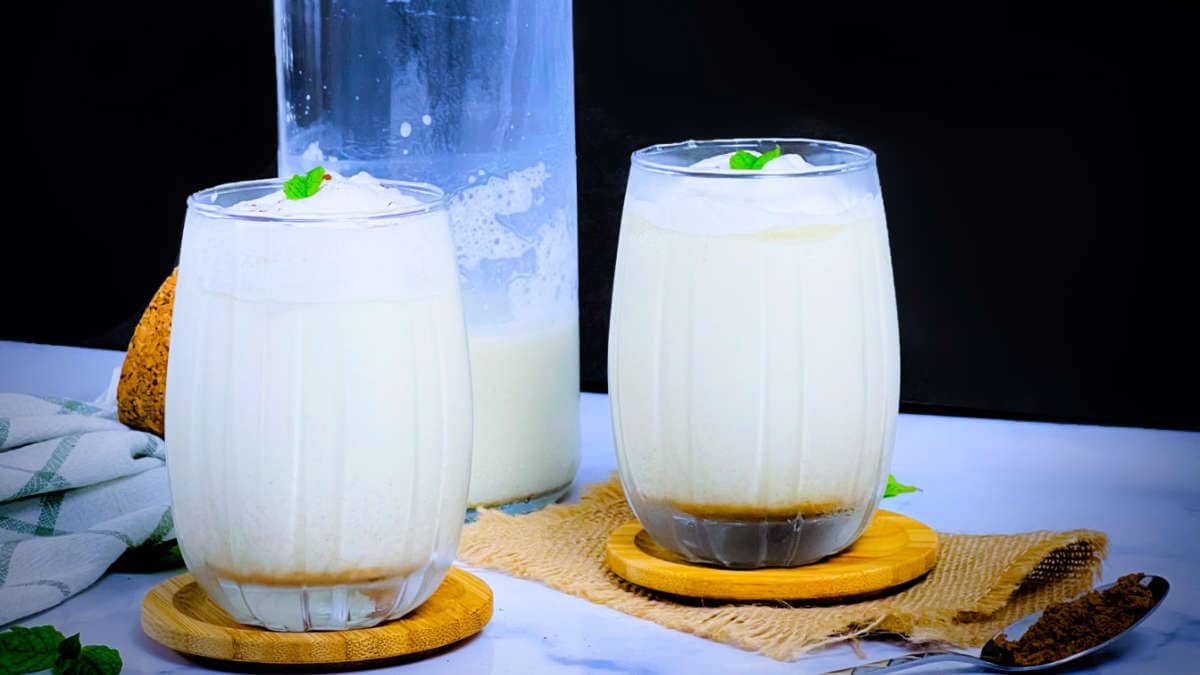 Two glasses of salted lassi placed on wooden coasters with lassi bottle in the background.