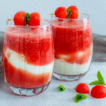 Watermelon lassi in two glasses placed on a white surface.